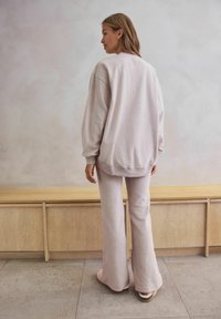 Jasnoróżowy, miękki, oversize'owy sweatshirt i rozszerzane spodnie. Prosty design z prążkowanymi mankietami i luźnym krojem. Gładka tekstura.