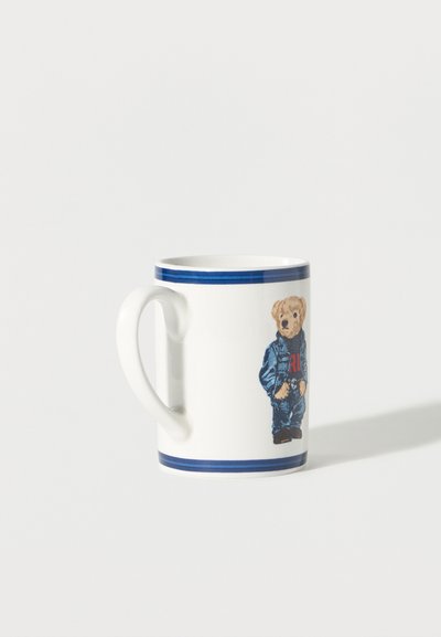 Λευκή κεραμική κούπα με μπλε ρίγες στην άκρη και εικονογράφηση ενός αρκουδάκι που φοράει τζιν μπουφάν και παντελόνι.