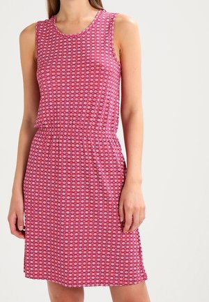 Różowa sukienka bez rękawów z małym białym kwiatowym wzorem, z elastycznym pasem, noszona przez stojącą osobę na jednolitym jasnym tle.