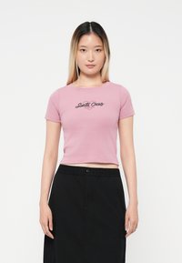 Kratka ružičasta majica s crnim "Santa Cruz" grafikonom na prednjoj strani, s kratkim rukavima i okruglim izrezom.