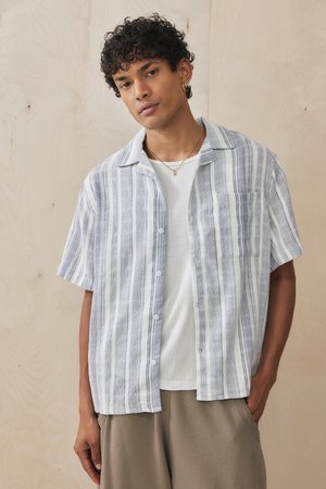 Short-sleeve, button-up shirt in light blue and white stripes. Made of a textured fabric, features a left chest pocket and relaxed fit.