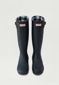 Botas de lluvia de goma navy con un acabado texturizado, que presentan un forro a cuadros y parches con el logo a ambos lados. Detalle de hebilla ajustable en el lateral.