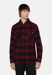 Camisa de franela a cuadros en rojo y negro con cuello, dos bolsillos en el pecho con solapa y cierre de botones en el frente. Fabricada con tela texturizada.
