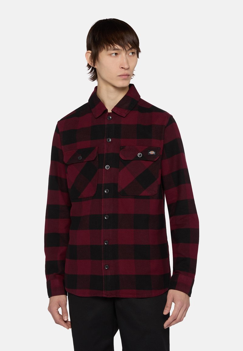 Camisa de franela a cuadros en rojo y negro con cuello, dos bolsillos en el pecho con solapa y cierre de botones en el frente. Fabricada con tela texturizada.