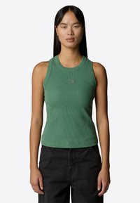 Top verde a costine con scollo tondo e logo discreto. Abbinato a pantaloni neri scuri, che mettono in evidenza un design aderente e una texture liscia.