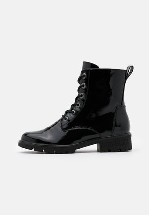 Czarny błyszczący skórzany botek na sznurowadła z masywną podeszwą i pętelką z tyłu, pokazany z profilu na jednolitym tle.