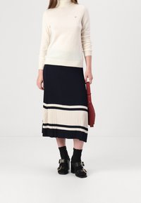 Krémový rolák, námořnická plisovaná sukně s krémovými a námořnickými pruhy, černé sandály na podpatku s kovovým sponou, červená kabelka.