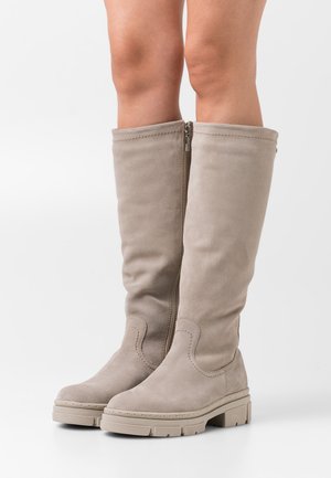 Bottes montantes beiges en daim lisse avec une semelle plate texturée et une fermeture éclair latérale. Présentent des surpiqûres discrètes pour plus de détails.