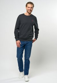 Hanorac gri închis cu manșete și tiv cu nervuri, având un mic logo roșu pe piept, asortat cu blugi albaștri și adidași albi.