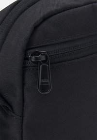 Zaino in tessuto nero con una superficie liscia, dotato di una zip SBS e cuciture visibili lungo le cuciture, che evidenziano la durata.
