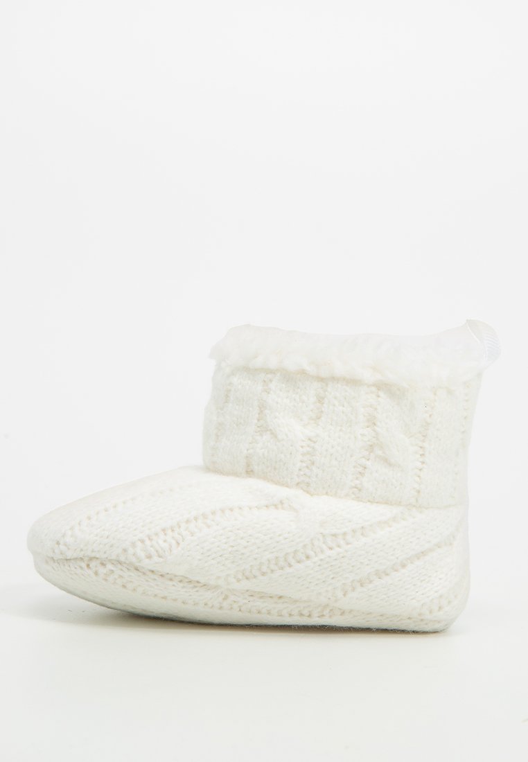 Botte de chausson tricotée blanche avec un motif texturé et un bord en fausse fourrure en haut. Matériau doux, bout arrondi et design profil bas.