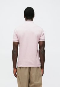 Trumpomis rankovėmis polo marškinėliai šviesiai rožinės spalvos, pagaminti iš medvilnės su tekstūruotu paviršiumi. Su apykakle ir kontrastinga balta apdaila rankovėse.