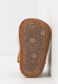 Brun ruskindssofa med en struktureret gummibund, der har gentagne brandmønstre og solstråledesign for bedre greb.