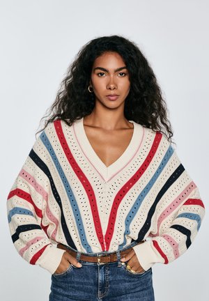 Sweter robiony na drutach z dekoltem w serek, dużymi rękawami, w kremowym kolorze z pionowymi paskami w kolorach czerwonym, niebieskim, różowym i granatowym oraz detalami w ażurowym wzorze.