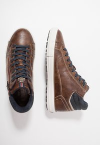 Brown leather high-top sneakers with navy textile accents, white rubber sole, and blue laces. Features a side zipper and contrasting stitching.