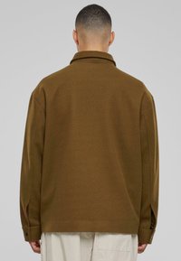 Brown, heavyweight collared shirt jacket with long sleeves, featuring side slits and buttoned cuffs. Smooth texture, relaxed fit.