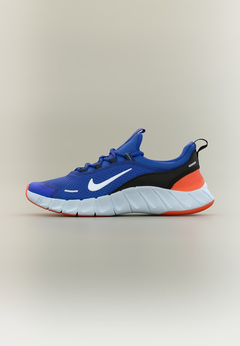 Μπλε αθλητικό παπούτσι Nike με λευκή σήμα, μαύρες και πορτοκαλί λεπτομέρειες και λευκή σόλα με τμήματα, εμφανιζόμενο σε πλάγια όψη σε ουδέτερο φόντο.