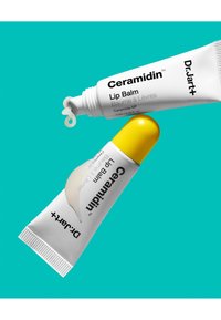 Tubes de baume à lèvres blanc et jaune avec un embout flexible, dotés de bouchons texturés et d'une crème lisse qui suinte de l'ouverture, sur un fond turquoise.