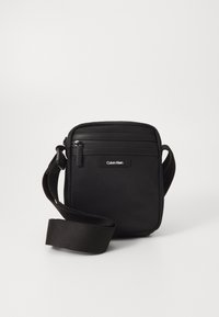 Borsa a tracolla nera in tessuto testurizzato, con due scomparti con zip e una tracolla regolabile. Logo Calvin Klein sulla parte anteriore.