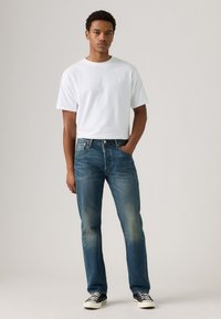 White crewneck T-shirt, blue straight-leg jeans with faded accents, and black low-top sneakers. Simple design, cotton fabric, and relaxed fit.