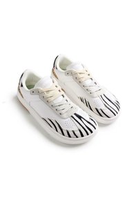 Zapatillas blancas con diseño a rayas negras y blancas en la puntera, detalles texturizados y cordones beige. Suela de goma lisa con detalles sutiles.