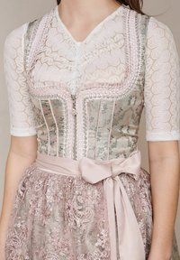 Vrouw in een roze en zilver geborduurde dirndl met een kanten blouse, een strik in de taille en bloemenpatronen op het lijfje en de rok.