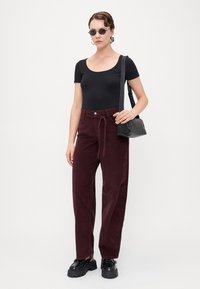 Sort tætsiddende bodysuit, bordeaux kordfløjl brede bukser med snoretræk i taljen, sort sling taske, klumpede sorte sko, runde solbriller.