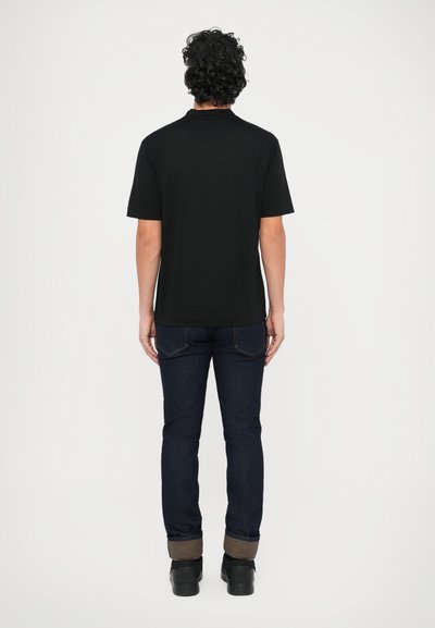 Fekete, rövid ujjú póló kerek nyakkal, sötétkék farmerrel és fekete cipővel viselve, egyszerű és minimalista dizájnt mutatva.