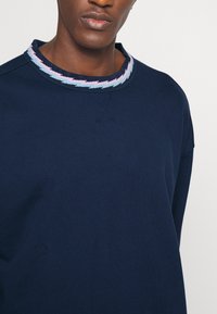 Felpa blu navy con un design testurizzato, caratterizzata da un colletto decorato in tonalità pastello. Realizzata in un tessuto morbido, presenta una vestibilità rilassata.