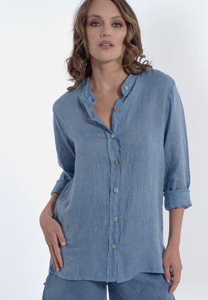 Chemise en lin bleu clair, à boutonner, avec une coupe décontractée, présentant un col montant, des manches retroussées et un dos légèrement plus long.