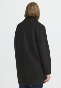 Cappotto nero strutturato con una vestibilità più ampia, dotato di colletto e spalle scese, rifinito con spacchi laterali e maniche lunghe.