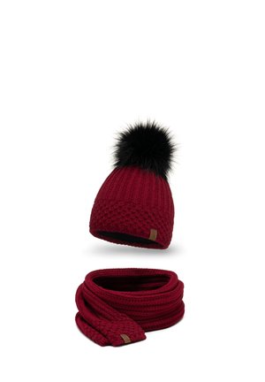 Rote gestrickte Mütze mit einem schwarzen Pelzbommel und einem passenden gestrickten Schal, der ein strukturiertes Muster und ein kleines Markenetikett aufweist.