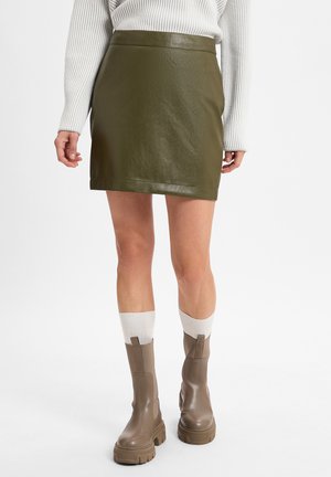 Olivengrønn faux skinn mini-skirt med en glatt tekstur, høy midje og rett snitt. Kombinert med brune kraftige ankel støvler og hvite sokker.