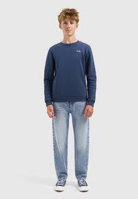 Marineblauwe sweatshirt met ronde hals, geribbelde manchetten en logo. Gecombineerd met lichtblauwe denimjeans en blauwe sneakers met witte zolen.