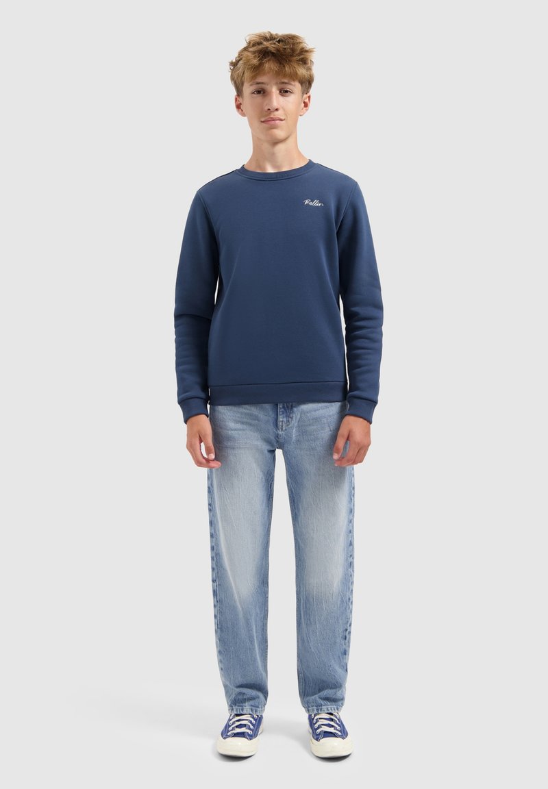 Marineblauwe sweatshirt met ronde hals, geribbelde manchetten en logo. Gecombineerd met lichtblauwe denimjeans en blauwe sneakers met witte zolen.