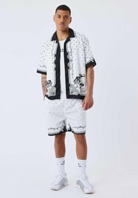 Camisa de manga corta en blanco y negro con un patrón, acompañada de pantalones cortos a juego, que presentan diseños gráficos, lunares y acentos negros contrastantes.