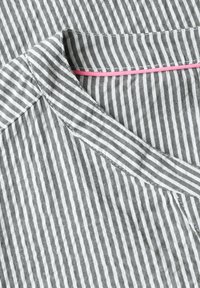 Grå och vit randig tyg med V-ringad krage, med en rosa accenterad ögla. Texturerad med en lätt, andningsbar väv.