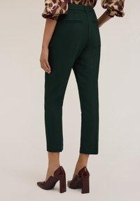Groene op maat gemaakte enkellange broek met een slanke pasvorm, voorzien van twee achterzakken en een soepele textuur; gecombineerd met bordeauxrode hoge hakken.