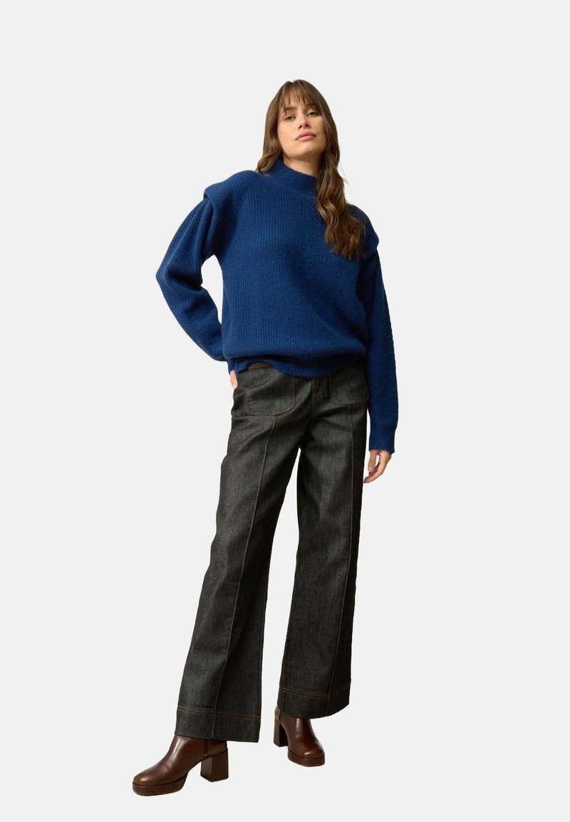 Niebieski sweter dzianinowy z lekko bufiastymi rękawami, w połączeniu z ciemnoniebieskimi, szerokimi spodniami o wysokim stanie i brązowymi kozakami na platformie.