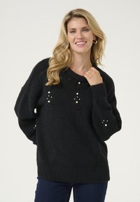 Melna adīta džemperis ar apaļu kaklu, ar dekoratīvām pērlītēm priekšpusē un uz piedurknēm, kā arī ar ribotām piedurknēm un apakšmalu, lai piešķirtu struktūru.