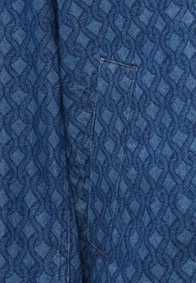 Tela de mezclilla con un patrón texturizado azul que presenta un diseño geométrico repetido. Incluye un pequeño bolsillo de parche en el costado.