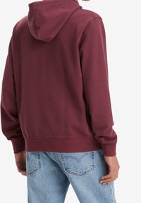 Bordó mikina s kapucí na šňůrku, manžety a lem s žebrováním, v kombinaci se světle modrými džínami. Hladká textilie, ležérní design.
