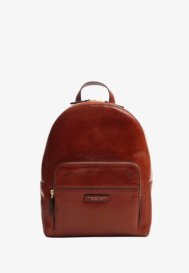 Zaino in pelle marrone dalla forma arrotondata, con tasca frontale con zip e maniglia superiore. Presenta dettagli di cucitura e un'etichetta con logo.