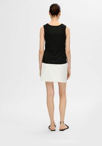 Svart ärmlös topp med en rundad halsringning, kombinerad med en vit minikjol. Outfiten har en enfärgad textur och en minimalistisk design.