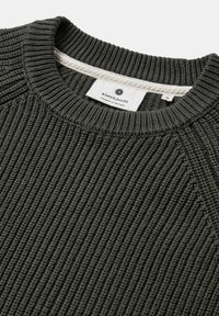 Maglione verde scuro a coste in maglia con scollatura rotonda e maniche raglan. L'etichetta mostra il nome del marchio e le istruzioni per la cura vicino al collo.