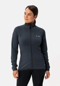 Giacca zip-up grigia scura con colletto alto, tessuto texturizzato e due tasche laterali. Presenta un logo bianco sul petto e un dettaglio verde all'orlo.