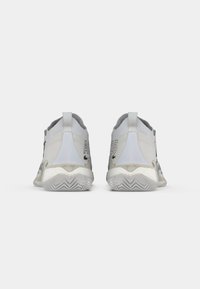 Ανοιχτό γκρίζα αθλητικά παπούτσια με λεία υφή, στρογγυλή μορφή, διχρωμία και μαύρες λεπτομέρειες που περιλαμβάνουν λογότυπο και αριθμό στυλ.