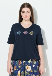 Camiseta de marina con mangas cortas y escote en V. Presenta flores bordadas en azul, rosa y amarillo en el centro. Textura de tela suave.