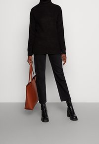 Maglione nero a coste con colletto a imbuto, abbinato a pantaloni neri dritti e stivaletti neri con tacco. Tiene una borsa a tracolla marrone con manici piatti.