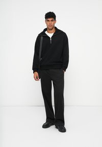 Zwarte sweatshirt met rits en een relaxed fit, gecombineerd met zwarte wijde broek en zwarte sneakers. Minimalistisch ontwerp, geen opvallende patronen.